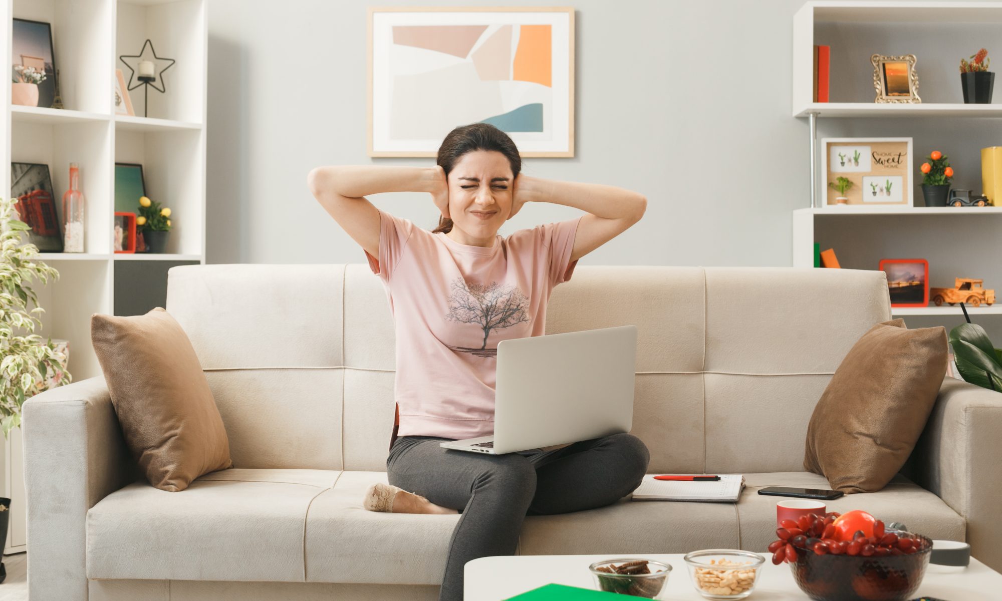 Young tenant blocks her ears, sitting on couch in her living room of rental property